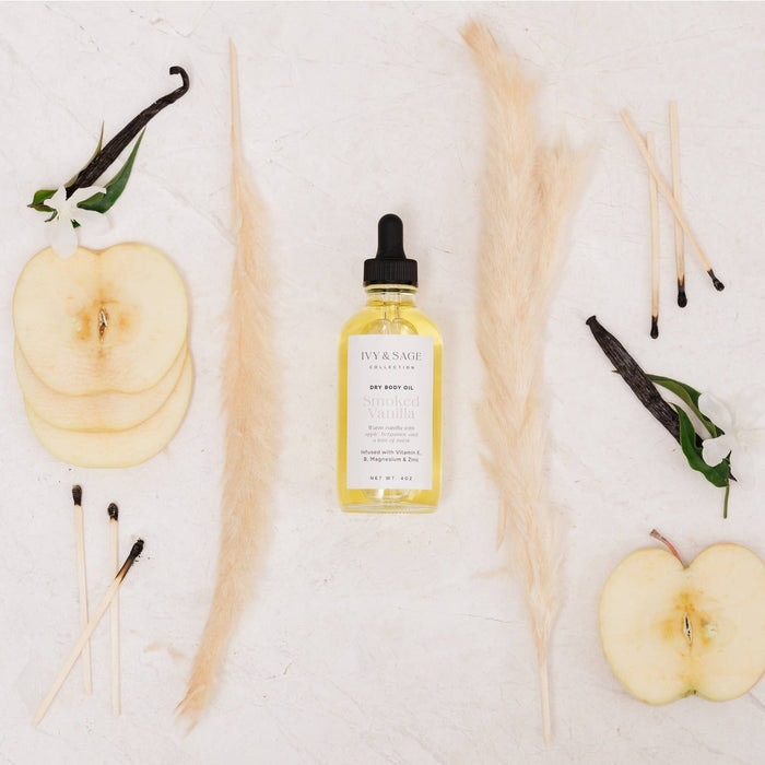 IVY & SAGE Dry Body Oil Smoked Vanilla displayed with apples, vanilla pods, and pampas grass on white background