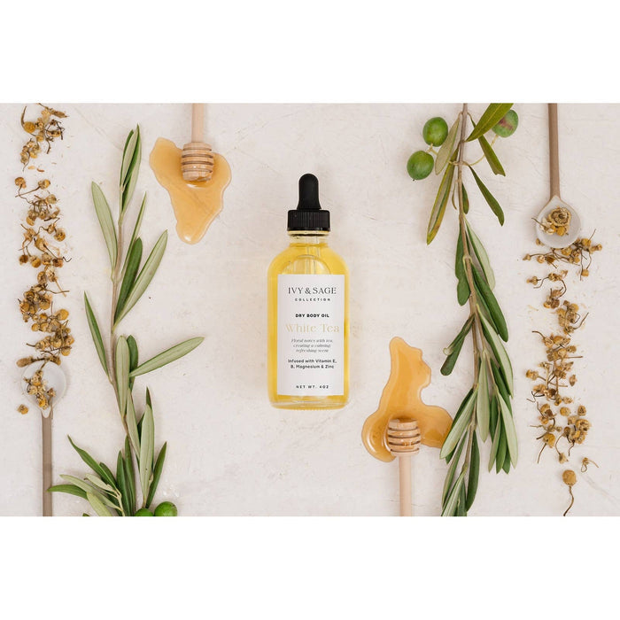 IVY & SAGE White Tea dry body oil bottle surrounded by natural ingredients and botanical elements on neutral background