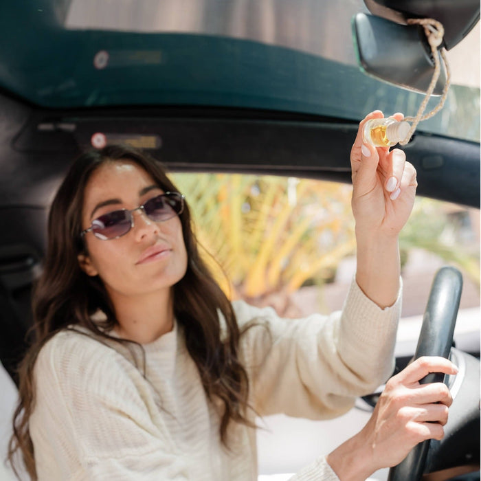 Woman holding Satsuma car diffuser in convertible, showcasing citrus fragrance accessory in use