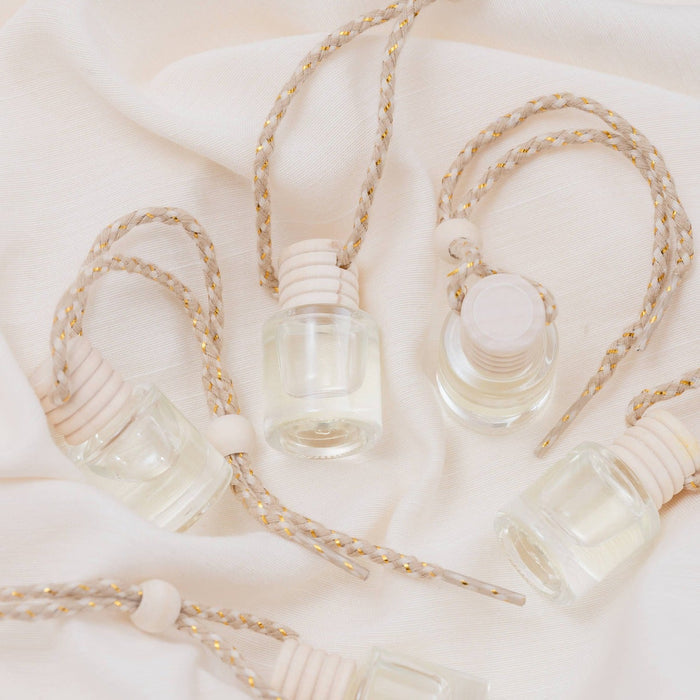 White Tea Car Diffuser bottles with jute rope hangers on cream fabric background