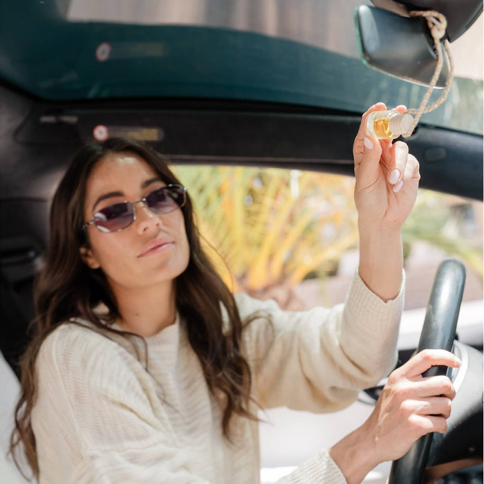 Woman holding White Tea car diffuser in convertible car, demonstrating fresh floral fragrance use while driving