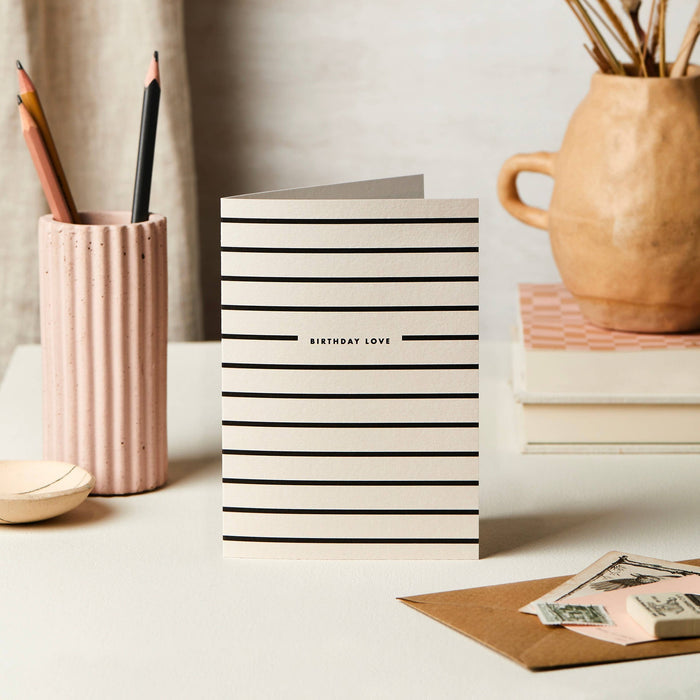 Katie Leamon Stripe Birthday Love greeting card displayed on white desk with stationery and flowers