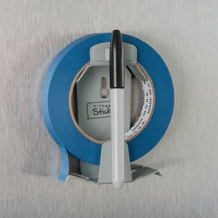 A roll of blue painter's tape mounted on a gray wall, via a kitchen sticken mount with a black-and-white marker resting on top.