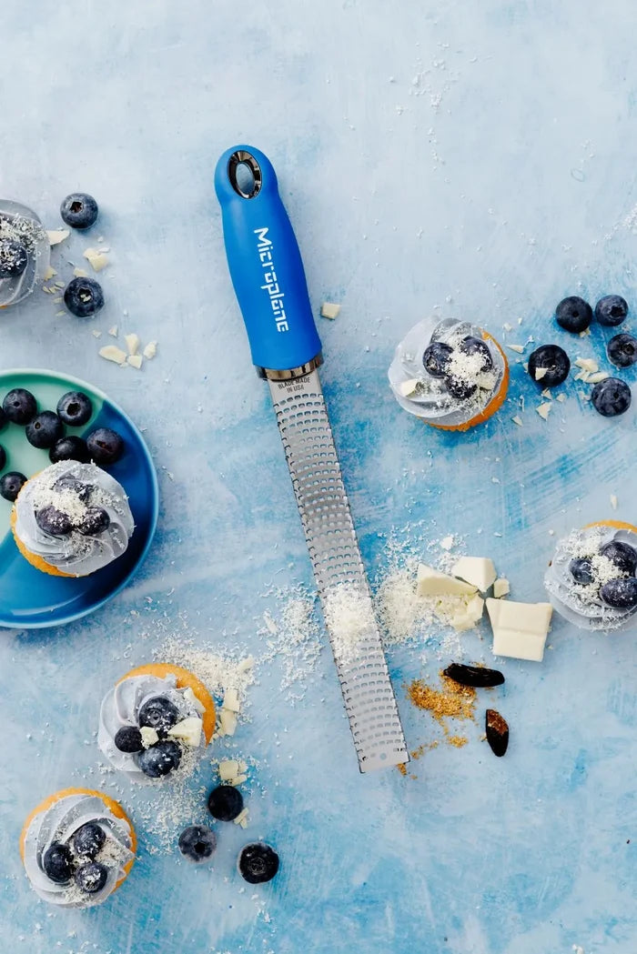 Microplane grater on a blue surface with cupcakes and blueberries