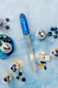 Microplane grater on a blue surface with cupcakes and blueberries