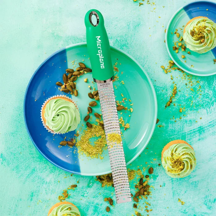 Microplane grater on a plate with green cupcakes and pistachios