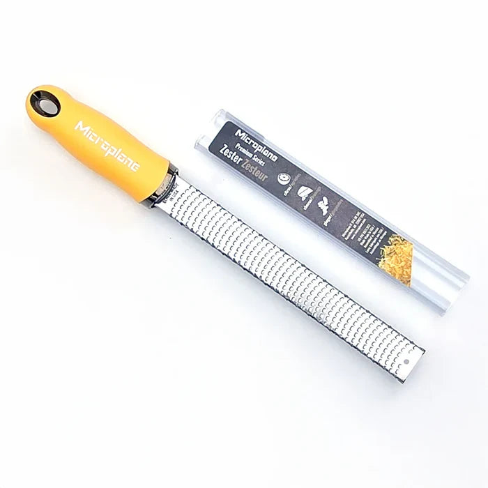 Metal zester with yellow handle and packaging on a white background