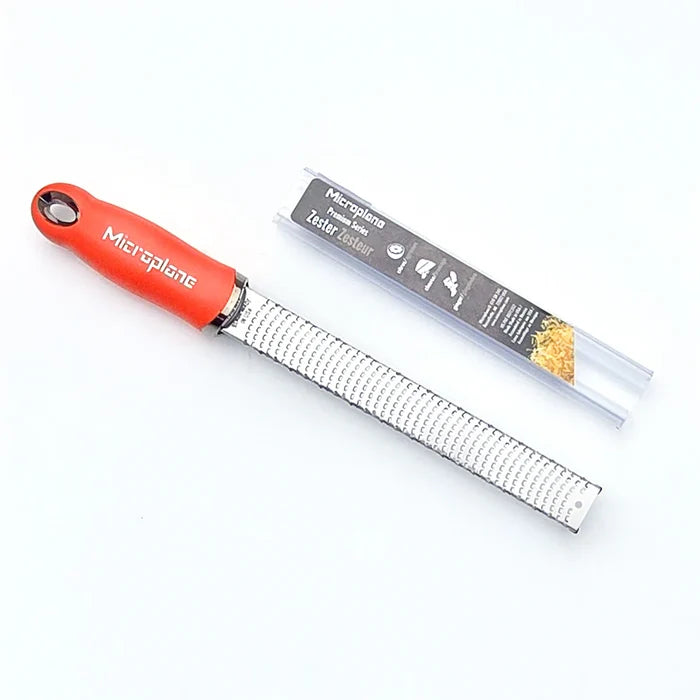 Metal zester with red handle and packaging on a white background