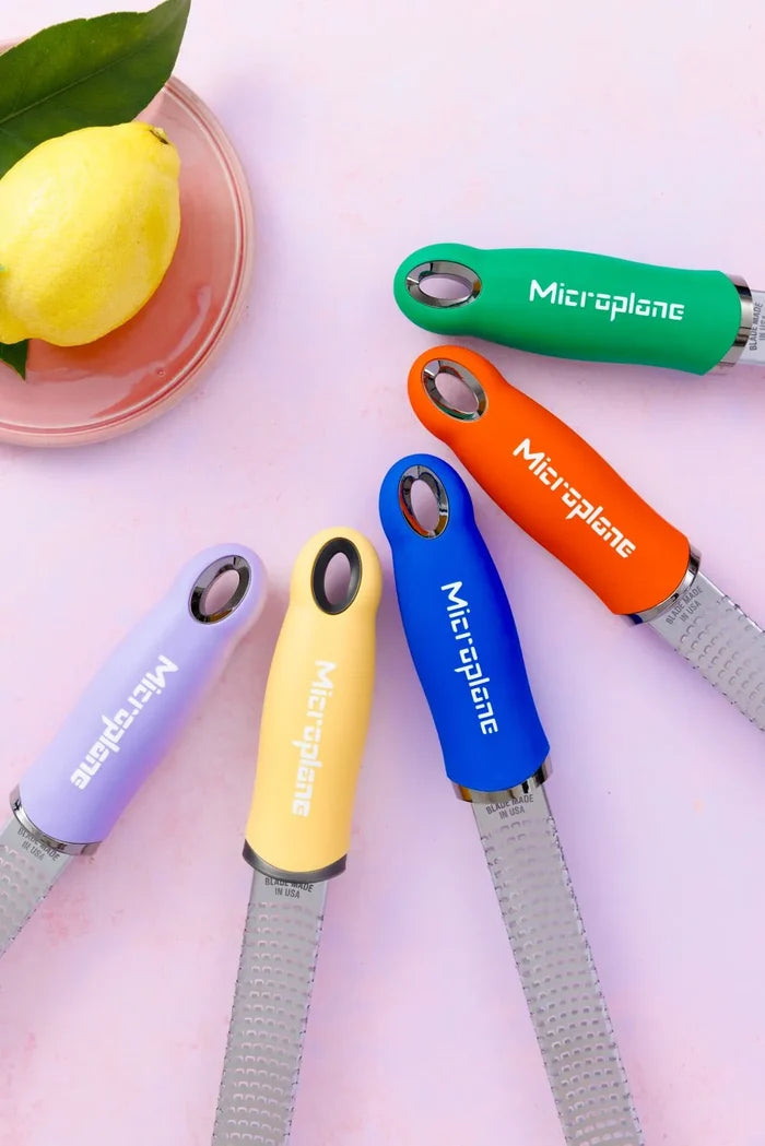 Colorful Microplane zesters on a pink surface with a lemon.