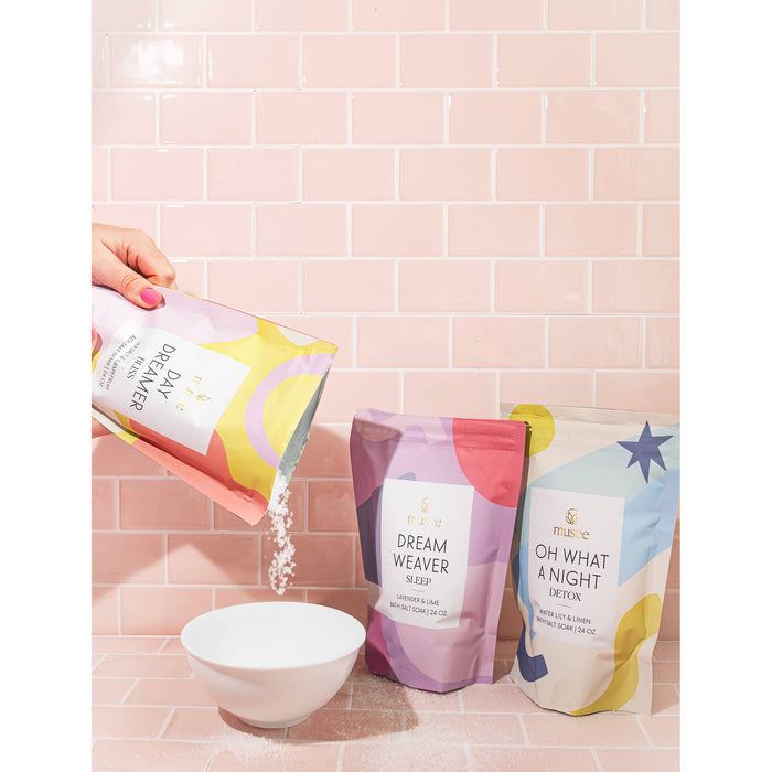 Hand pouring Musee Daydreamer bath salt soak into white bowl with colorful product packaging displayed