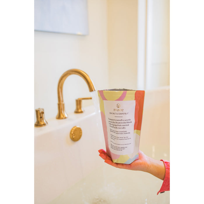 Sea salt grapefruit bath soak held in bathroom setting with gold faucet