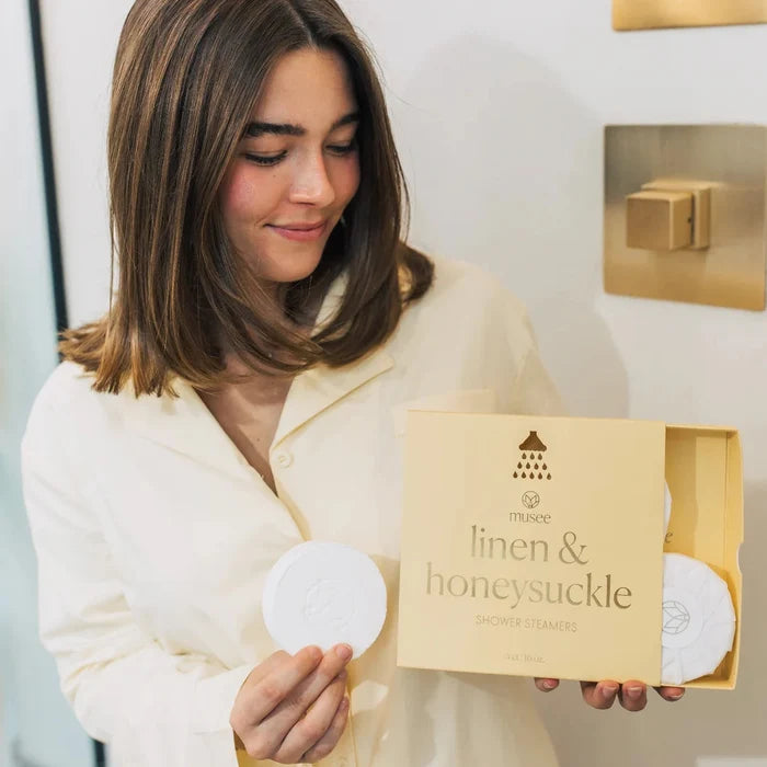 Woman holding a box of 'Linen & Honeysuckle' shower steamers in a neutral setting