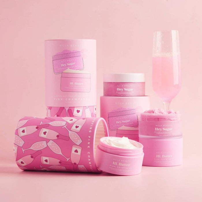 NCLA Beauty Pink Champagne Body Scrub and Body Butter Set with cosmetic bag on pink background
