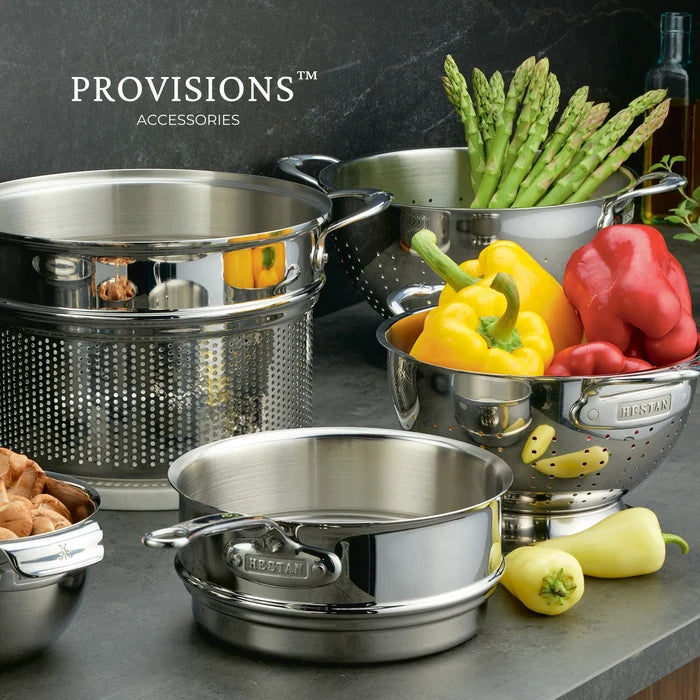 Stainless steel cookware set with vegetables on a dark surface, featuring the 'Hestan' provisions brand line.