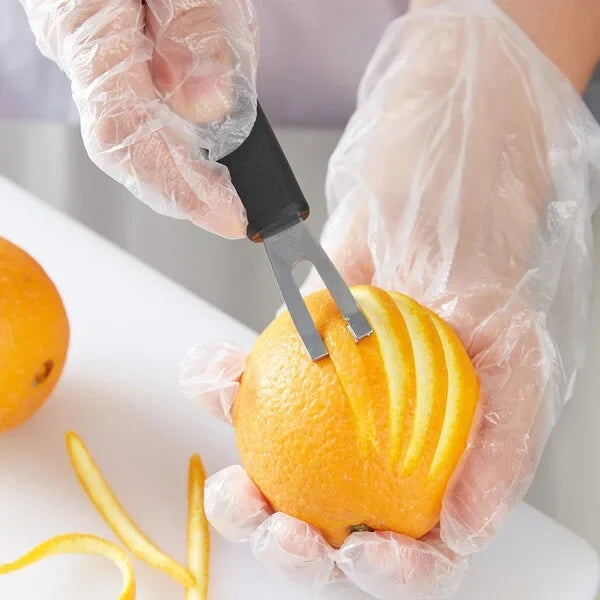 Person using a channel knife to remove orange skin on a white surface.